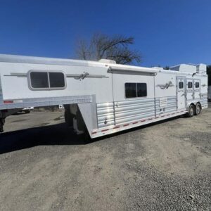 A used 2009 Platinum Coach 3-horse gooseneck trailer with a 16-foot living quarters, featuring a custom Outlaw Conversion. The trailer has a polished aluminum exterior with graphics and a hay rack on top.