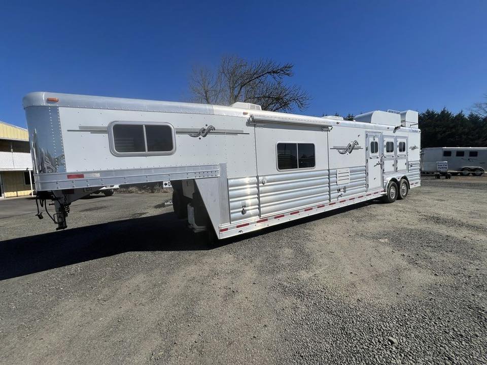 2009 Platinum Coach 3 H 16’ LQ with Outlaw Conversion 1 A used 2009 Platinum Coach 3-horse gooseneck trailer with a 16-foot living quarters, featuring a custom Outlaw Conversion. The trailer has a polished aluminum exterior with graphics and a hay rack on top.