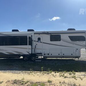 A large, white and gray 2025 Jayco North Point 377RLBH fifth wheel RV, a luxury model with a distinctive front cap and multiple extended slide-outs. The RV is shown in an outdoor setting, highlighting its expansive size and residential feel.