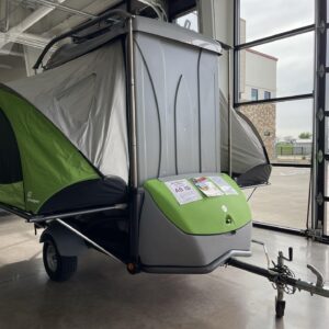 A 2017 Sylvan Sport GO, a versatile and lightweight pop-up camping trailer. The trailer is shown in its compact, travel-ready state, with a streamlined, gray-and-green design. It has a cargo rack on top and is low-profile for easy towing.