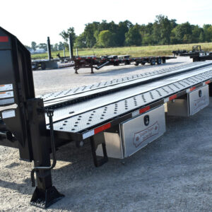 A long, gray 53-foot gooseneck trailer, a flatbed style trailer designed for heavy hauling. The trailer has tandem axles and a low-profile deck, and is shown in a clean, industrial setting, highlighting its immense length.