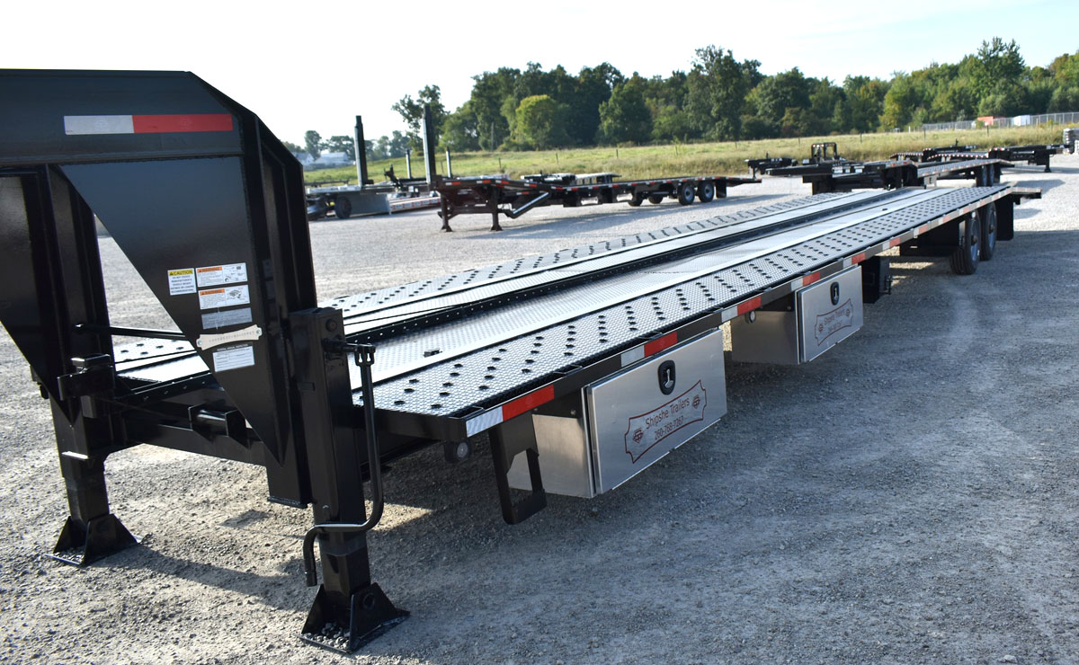 Shipshe 53′ Gooseneck Trailer 1 A long, gray 53-foot gooseneck trailer, a flatbed style trailer designed for heavy hauling. The trailer has tandem axles and a low-profile deck, and is shown in a clean, industrial setting, highlighting its immense length.