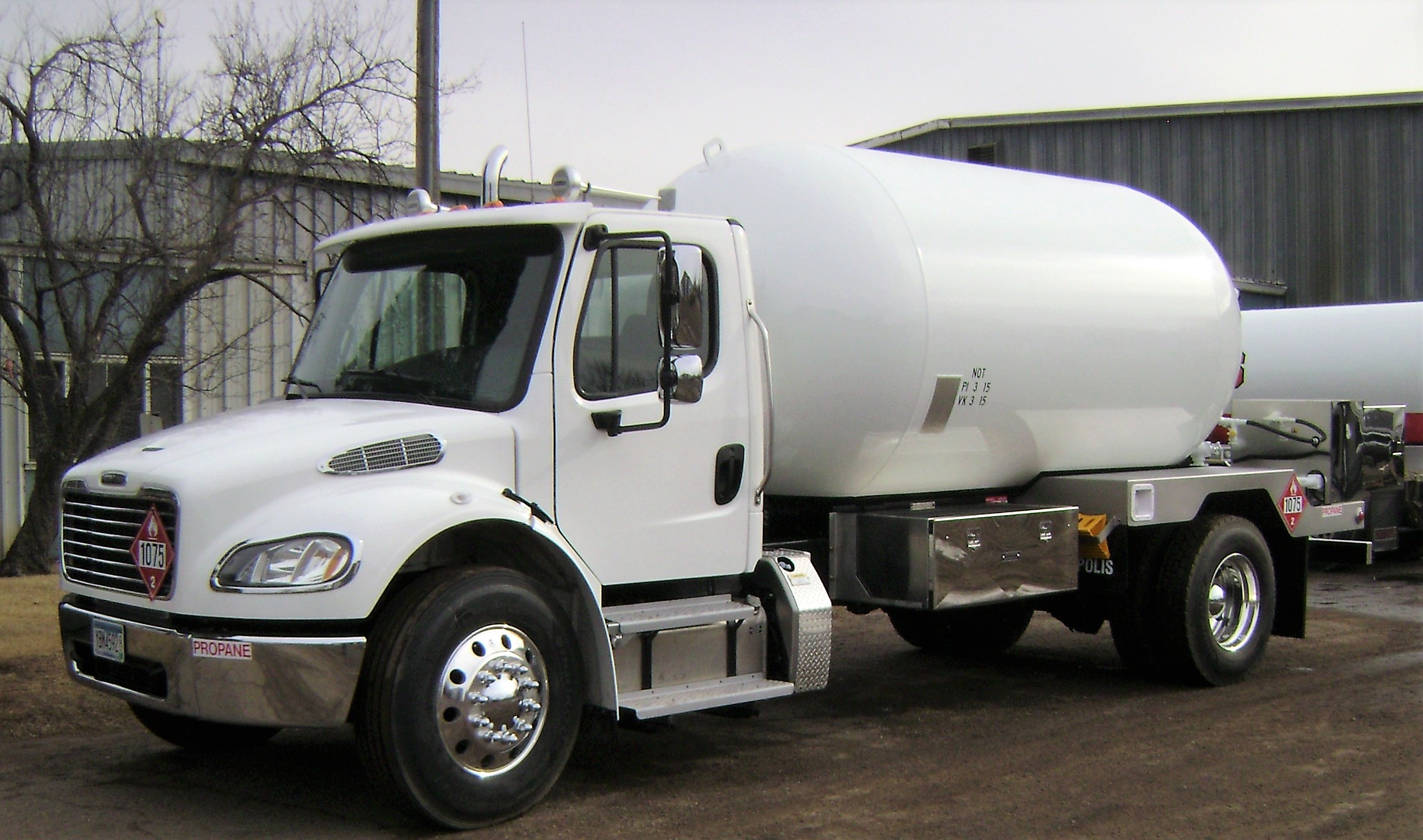 Buy Blueline BX Bobtail Trucks Online 1 A Blueline BX Bobtail propane delivery truck, featuring a large cylindrical tank mounted on a truck chassis. The tank is black or a dark color, with a hose reel and other delivery equipment visible at the rear.