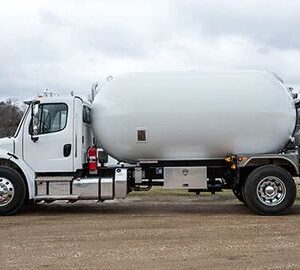 A Blueline QX Bobtail propane delivery truck, shown from a side view. The truck is a large industrial vehicle with a prominent cylindrical propane tank mounted on its chassis. A hose reel and control panel are visible at the rear of the tank. The tank and truck cab appear to be a dark color.